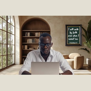 Może przedstawiać: Osoba w okularach i białej koszuli pracuje na laptopie w domowym biurze. Oprawiony wydruk na ścianie głosi: „Będę chodził przez wiarę, nawet jeśli nie mogę widzieć”. Widoczne jest duże okno i regał z książkami.