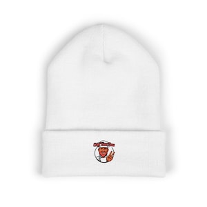 Peut inclure: Bonnet blanc avec bord replié. Le chapeau présente un logo brodé circulaire d'un chef faisant le signe de la paix, avec le texte "Chef Bardou" au-dessus de la tête du chef.