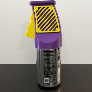 K&ouml;nnte beinhalten: Ein lila-gelber Dosen-Griff, der auf eine Getr&auml;nkedose passt. Der Griff hat einen Griff und ein gelbes Gittermuster auf der Oberseite. Die Dose ist silberfarben mit schwarzem Text.
