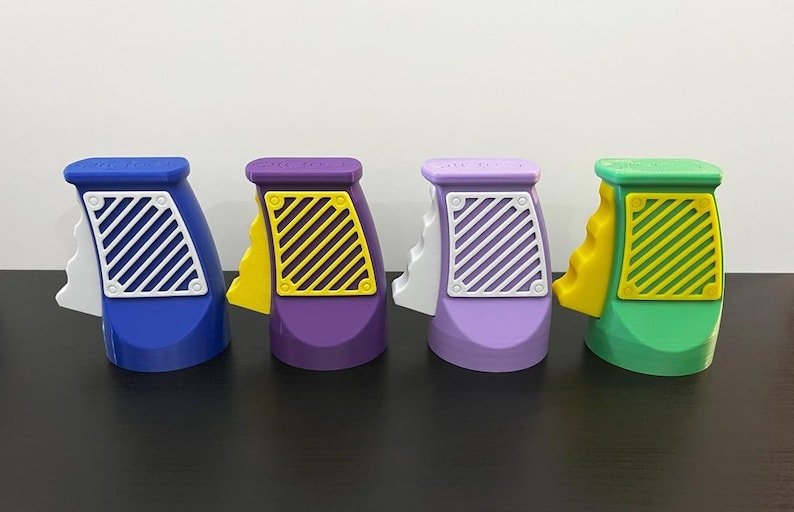 K&ouml;nnte beinhalten: Vier bunte Spielzeugpistolen in Blau, Lila, Lavendel und Gr&uuml;n. Jede hat einen wei&szlig;en und gelben Akzent mit einem diagonal gestreiften Design an der Seite. Die Spielzeuge sind in einer Reihe auf einer dunklen Oberfl&auml;che angeordnet.