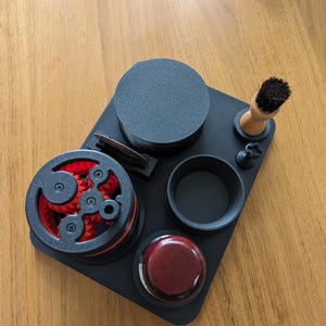 Peut inclure: Un plateau noir avec cinq compartiments pour les accessoires de toilettage. Le plateau a un motif d'engrenage rouge et noir dans un compartiment, une brosse noire dans un autre et une brosse en bois dans un troisième. Il y a un petit récipient noir et un récipient rouge dans les compartiments restants.