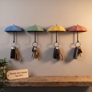 May include: A set of four wall-mounted key hooks shaped like miniature umbrellas in blue, green, yellow, and coral colours. Each hook features a black handle and a metal ring holding various keys. A wooden sign reads Nordic Key Hooks - Set of 4.