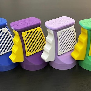 K&ouml;nnte beinhalten: Vier farbenfrohe, 3D-gedruckte Objekte in Blau, Lila, Lavendel und Gr&uuml;n. Jedes hat einen wei&szlig;en Griff, einen gelben Akzent und ein wei&szlig;es oder gelbes Gitter. Die Oberseiten haben Pfeile und kreisf&ouml;rmige Designs. Die Objekte stehen auf einer dunklen Oberfl&auml;che.
