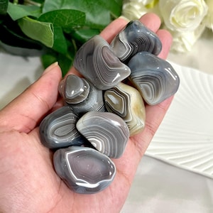 Peut inclure: Plusieurs pierres d'agate polies, aux tons gris, blancs et beiges. Les pierres présentent un motif en bandes et une forme lisse et arrondie. Les pierres sont naturelles et varient en taille et en couleur.