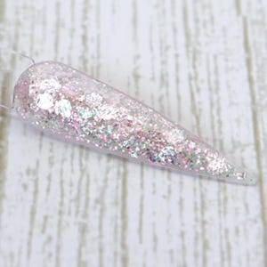 May include: A clear, pointed nail swatch filled with iridescent glitter. The glitter is a mix of pink, silver, and iridescent flakes, creating a sparkling effect. The swatch is held by a clear plastic stick, showcasing the nail art design.