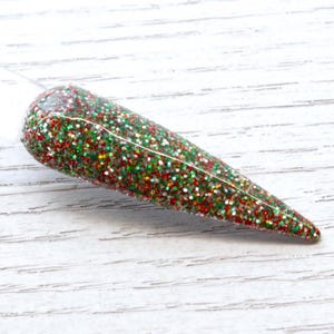May include: A close-up of a clear nail polish bottle with a green, red and silver glitter finish.
