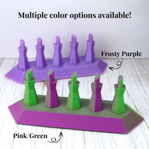 May include: Two hexagonal display stands with five vertical pegs each. The back stand is solid purple with the text Frosty Purple. The front stand features a purple base with alternating green and purple pegs, labeled with the text Pink/Green.