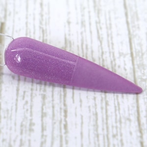 Pode incluir: Uma amostra de unha lavanda com acabamento brilhante na metade superior e acabamento fosco na metade inferior. A unha é segurada por um palito de plástico transparente, mostrando a cor e a textura do esmalte.
