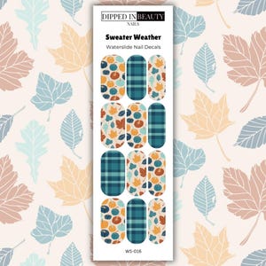 May include: A sheet of Sweater Weather waterslide nail decals featuring patterns of pumpkins, autumn leaves, and teal plaid. The packaging includes the brand name Dipped in Beauty Nails and the product code WS-016 printed on a white rectangular card.