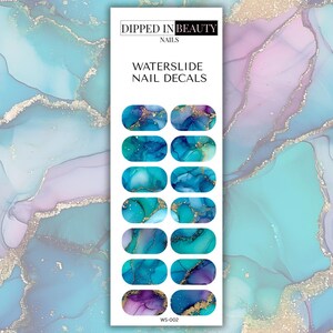 May include: Waterslide nail decals with abstract designs in shades of blue, teal, and purple, accented with gold. The package features the text "Dipped in Beauty Nails" and "Waterslide Nail Decals."