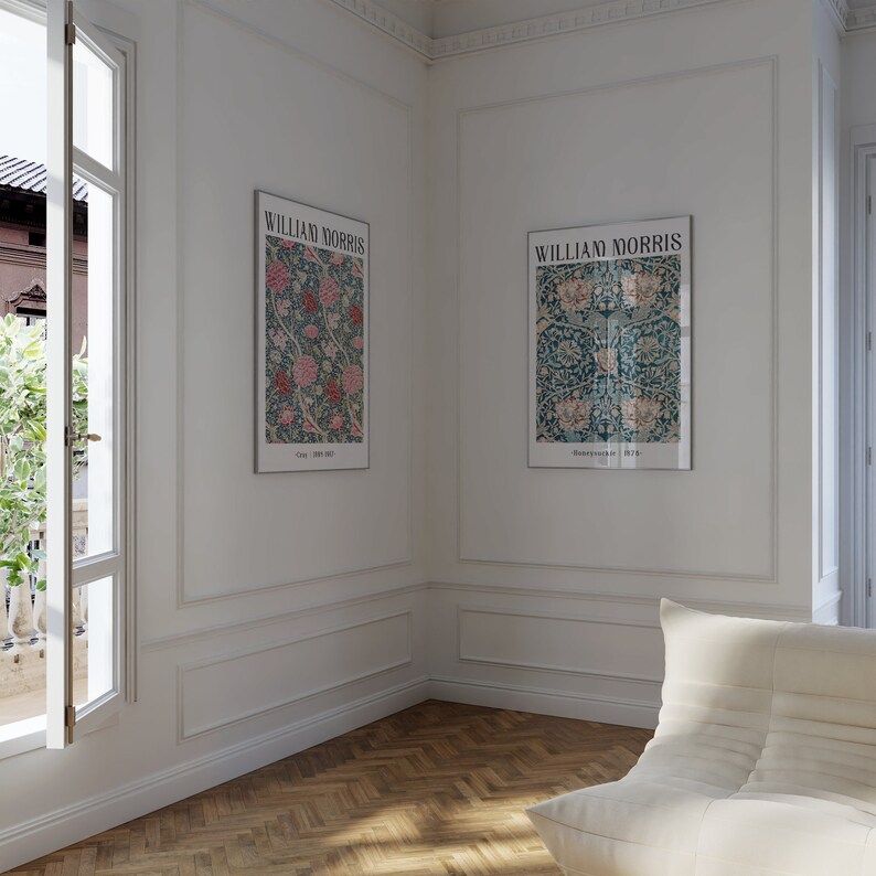 May include: Two framed prints of floral patterns by William Morris, one with a blue background and pink flowers, the other with a green background and white flowers. The prints are hanging on a white wall with white molding.