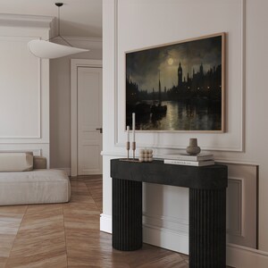 Pu&ograve; includere: Un tavolino da console nero con gambe scanalate, con un dipinto incorniciato di una citt&agrave; notturna con luna piena, due candelabri e una pila di libri in cima.