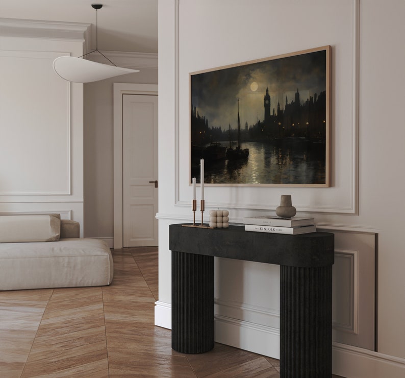 Pu&ograve; includere: Un tavolino da console nero con gambe scanalate, con un dipinto incorniciato di una citt&agrave; notturna con luna piena, due candelabri e una pila di libri in cima.