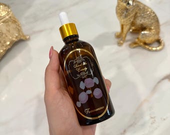 以下が含まれることがあります： 「Sweet like Candy」のラベルとキャンディーのイラストが入った、金色のキャップと白いスポイトが付いた茶色のガラス瓶。手で持っており、背景には金の猫の像がある。