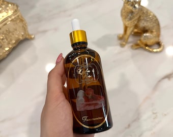 May include: A brown glass bottle with a gold cap and a white dropper. The bottle has a label with the text "Lychee & Rose" and "Femenina". The bottle is held in a hand.