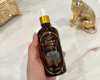 May include: A brown glass bottle with a gold cap and white dropper, labeled "Cinnamon Rolls" with a picture of a cinnamon roll. The bottle is held in a hand with pink nail polish. The word "Femmenina" is printed on the bottle.