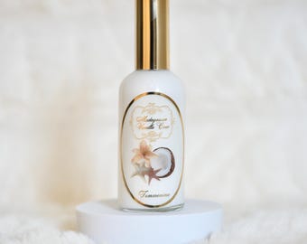 May include: A white bottle with a gold cap and a label that reads "Madagascar Vanilla Coco" with a flower and coconut illustration. The bottle is on a white pedestal against a soft, white background.