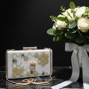 Pochette Worker Bee: pelle scamosciata bianca con ricamo dorato a nido d'ape, realizzata a mano.