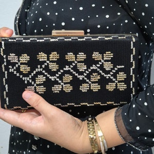 Könnte beinhalten: Eine schwarze Clutch mit goldenem Verschluss und einem gold- und silberfarbenen Stickmuster.