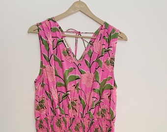 May include: A pink sleeveless dress with a floral print. The dress has a gathered waist and a tiered skirt.
