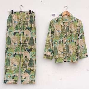 Op de afbeelding: Een groene en beige pyjamaset met een botanische print met bomen, vogels en koepels. De set bevat een shirt met lange mouwen met een knoopsluiting en een bijpassende broek.