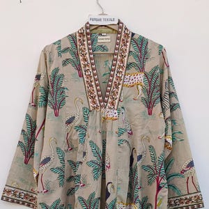 May include: A beige tunic with a V-neck and three-quarter sleeves. The tunic features a repeating pattern of palm trees, leopards, and birds. The neckline and sleeve cuffs have a decorative border. The tag reads "FUTURE TEXTILE".