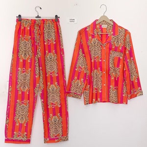 May include: Orange and pink striped pajamas with a tiger print. The pajamas have a button-up top with long sleeves and matching pants.