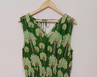 May include: A green sleeveless dress with a V-neck and a palm tree print. The dress has a gathered waist and a tiered skirt.
