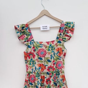 May include: A tiered floral print dress with a square neckline and ruffle sleeves. The dress is cream colored with red, pink, orange, and blue flowers. The dress has a tag that says "Future Textile".