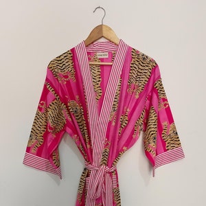 May include: A pink and white striped robe with a tiger print. The robe has a tie belt and long sleeves.