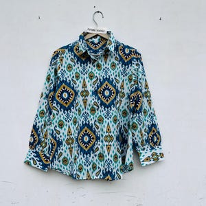 Op de afbeelding: Een overhemd met lange mouwen en knoopsluiting, voorzien van een herhalend geometrisch ikat-patroon in diepblauw, talinggroen en mosterdgeel op een witte achtergrond. Het overhemd heeft een standaard kraag en manchetten met een Future Textile label.