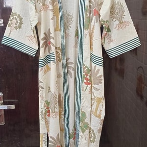 May include: A white cotton robe with a green and white striped trim. The robe has a floral print of trees and flowers.