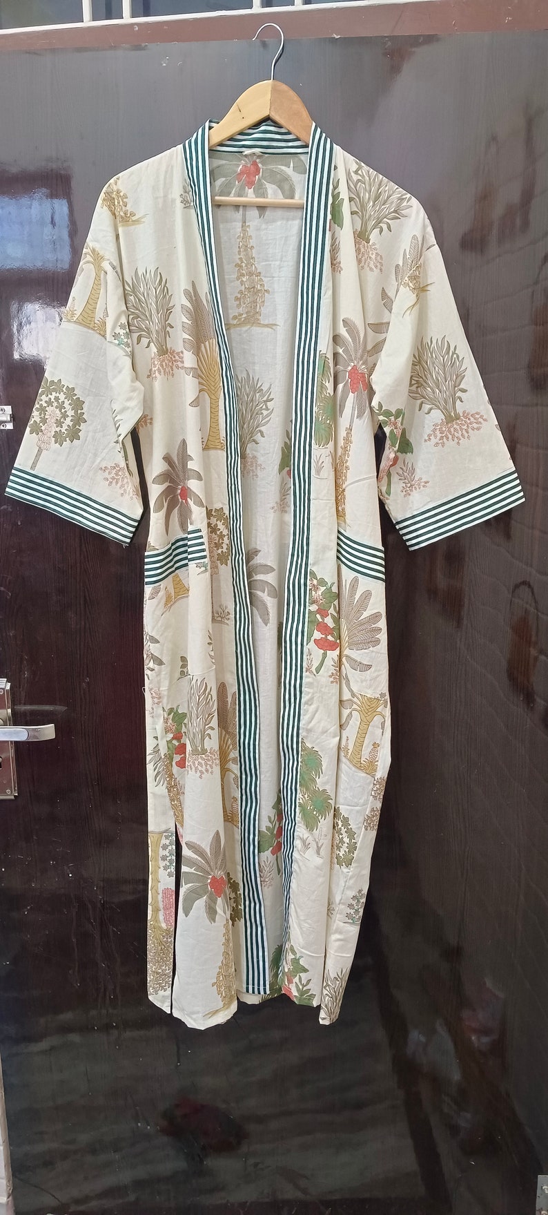 May include: A white cotton robe with a green and white striped trim. The robe has a floral print of trees and flowers.