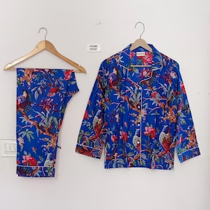 May include: Blue pajama set with a floral and bird print. The set includes a button-down shirt and matching pants, both trimmed with white piping. The shirt and pants are hanging on wooden hangers. The text "FUTURE TEXTILE" is visible.