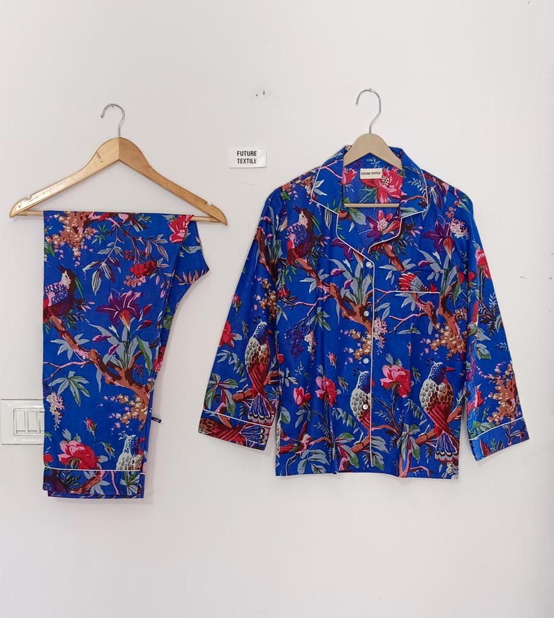 May include: Blue pajama set with a floral and bird print. The set includes a button-down shirt and matching pants, both trimmed with white piping. The shirt and pants are hanging on wooden hangers. The text "FUTURE TEXTILE" is visible.
