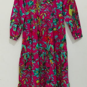 May include: A long-sleeved pink dress with a floral print featuring birds and leaves. The dress has a ruffled hem and a button-up collar.