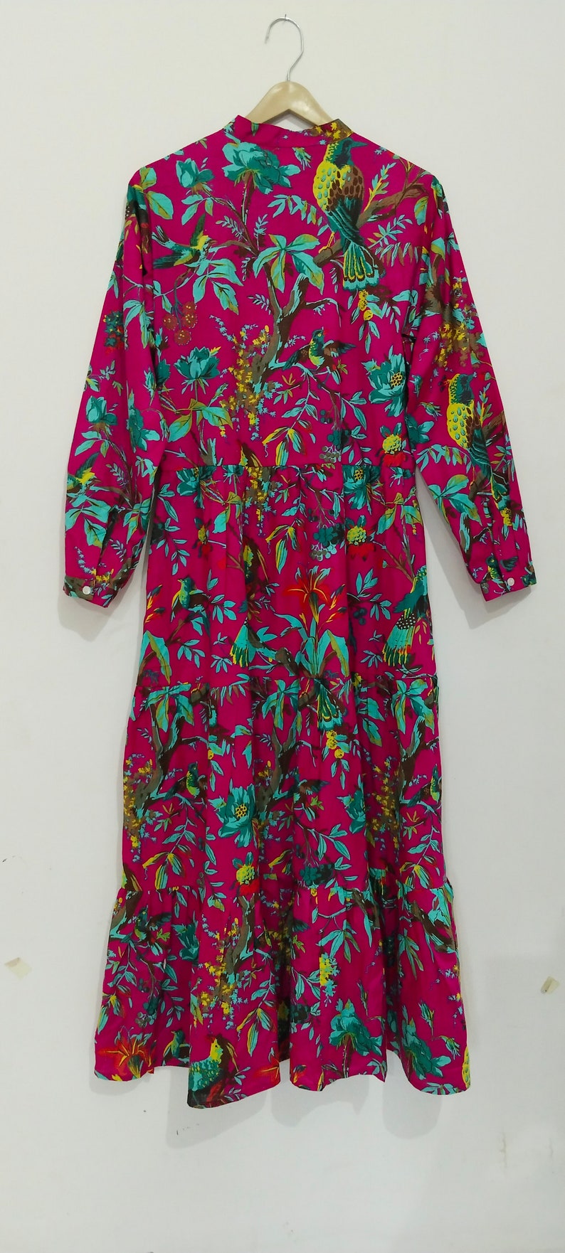 May include: A long-sleeved pink dress with a floral print featuring birds and leaves. The dress has a ruffled hem and a button-up collar.