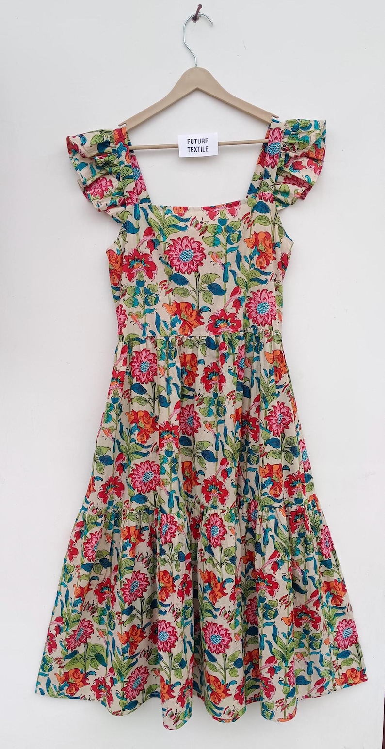 May include: A tiered floral print dress with a square neckline and ruffle sleeves. The dress is cream colored with red, pink, orange, and blue flowers. The dress has a tag that says "Future Textile".