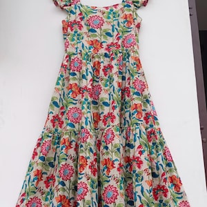 May include: A tiered maxi dress with a floral print in shades of pink, red, orange, blue, and green. The dress has a square neckline and ruffled straps. The dress is hanging on a hanger with a tag that reads "Future Textile".