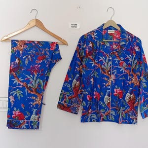 May include: Blue pajama set with a vibrant floral and bird print. The set includes a button-down shirt and matching pants. The shirt has white piping and the text "FUTURE TEXTILY".