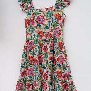 May include: A cream-colored midi dress with a floral print in shades of red, pink, blue, and green. The dress has a square neckline, ruffled straps, and a tiered skirt.