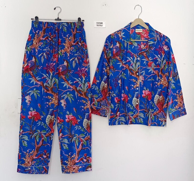 May include: Blue pajama set with a vibrant floral and bird print. The set includes a button-down shirt and matching pants. The fabric features red flowers, brown branches, and white trim. The pajamas are displayed on a white background.