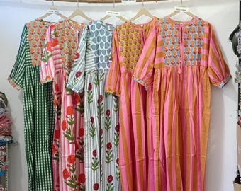 May include: Five colorful dresses hanging on a wooden rod. The dresses feature various patterns, including stripes, floral prints, and a checkered design. The color palette includes green, pink, orange, and blue. Each dress has a unique neckline and sleeve design.