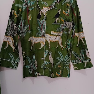 以下が含まれることがあります： 白い縁取りのある緑色のボタンダウンシャツ。シャツには、ヒョウ、オニオオハシ、ヤシの木が描かれたジャングル柄がプリントされています。シャツのラベルには「Future Textile」と書いてあります。