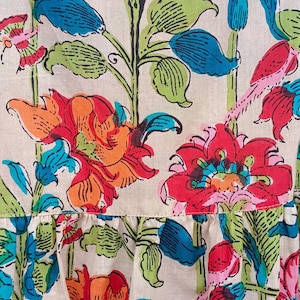 May include: A white fabric with a floral print featuring red, orange, pink, blue, and green flowers. The fabric has a ruffled edge.