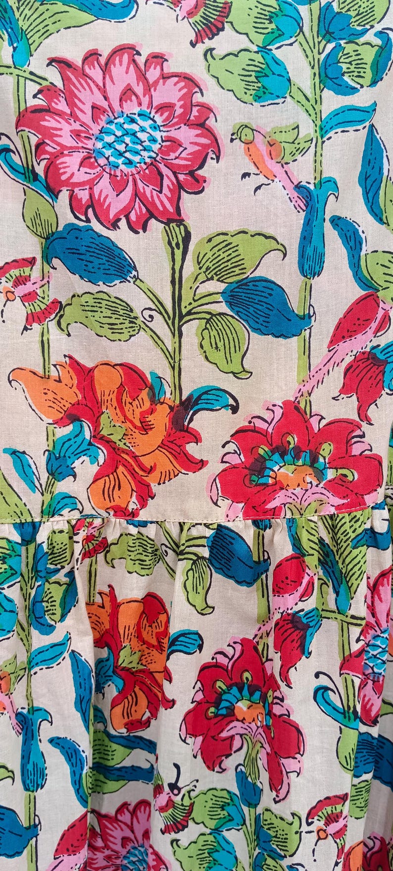 May include: A white fabric with a floral print featuring red, orange, pink, blue, and green flowers. The fabric has a ruffled edge.