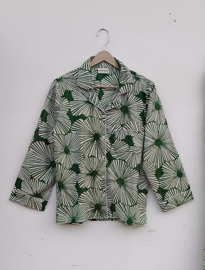 K&ouml;nnte beinhalten: Ein gr&uuml;n-wei&szlig;es Hemd mit Kn&ouml;pfen und einem floralen Muster. Das Hemd hat einen Kragen und lange &Auml;rmel. Das Hemd h&auml;ngt an einem Holzb&uuml;gel.