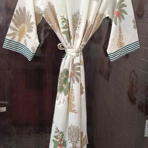 May include: A white cotton robe with a green and brown floral print. The robe has a tie belt and green and white striped trim on the sleeves.