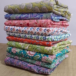 May include: A stack of ten colorful fabric panels with floral patterns. The fabric is folded and stacked on a wooden surface.
