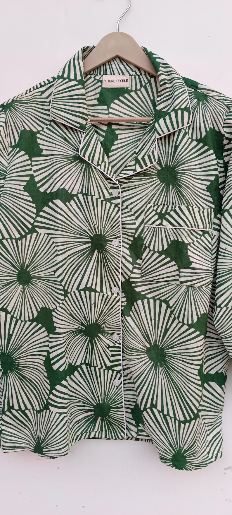 K&ouml;nnte beinhalten: Ein gr&uuml;n-wei&szlig;es Hemd mit Kn&ouml;pfen und einem floralen Muster. Das Hemd hat einen wei&szlig;en Saum um den Kragen und die Manschetten. Das Etikett auf dem Hemd lautet "FUTURE TEXTILE".